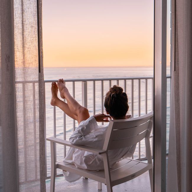 Woman sitting in chair on balcony overlooking ocean sunset