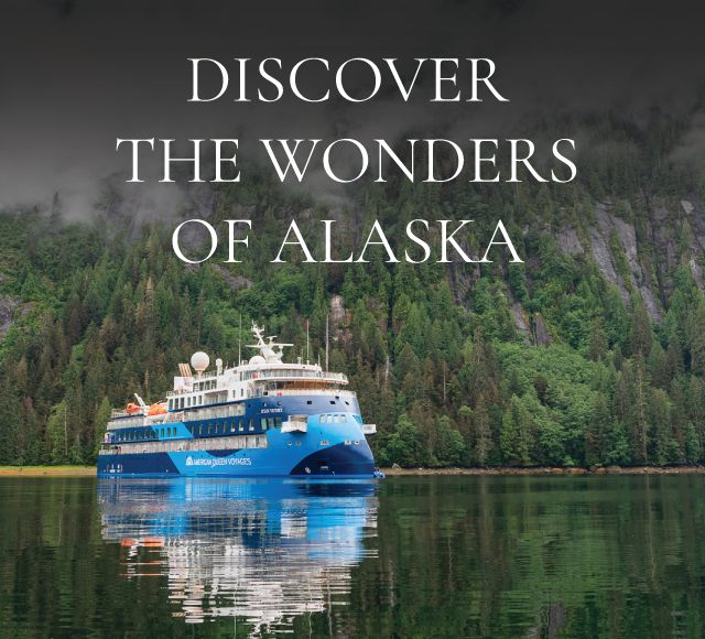 Cruise ship from American Queen Voyages on calm Alaskan waters with dense, green forests and misty mountains in the background, under the text 'DISCOVER THE WONDERS OF ALASKA'.