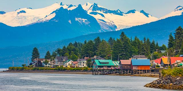 Scenic view of Petersburg, Alaska, with stilt houses along the waterfront and snow-capped mountains in the background.