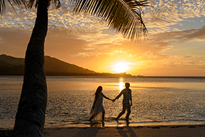 couple walking down coast overlooking sunset